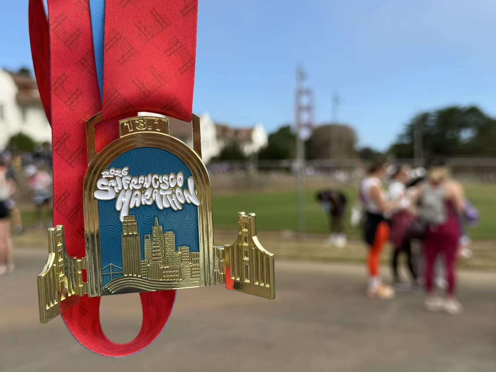 San Francisco Marathon finisher medal on a red ribbon, with the Golden Gate Bridge blurred in the background